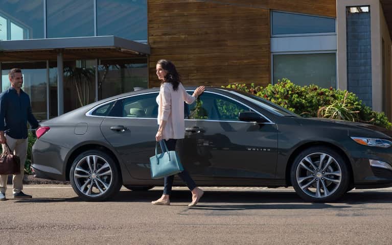 Woman holding large purse walking next to a vehicle outside