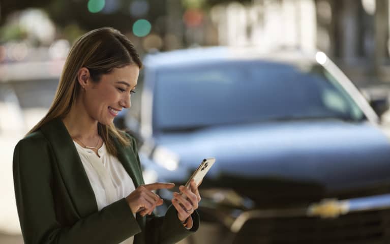 Woman looking at her phone and smiling near a chevrolet vehicle